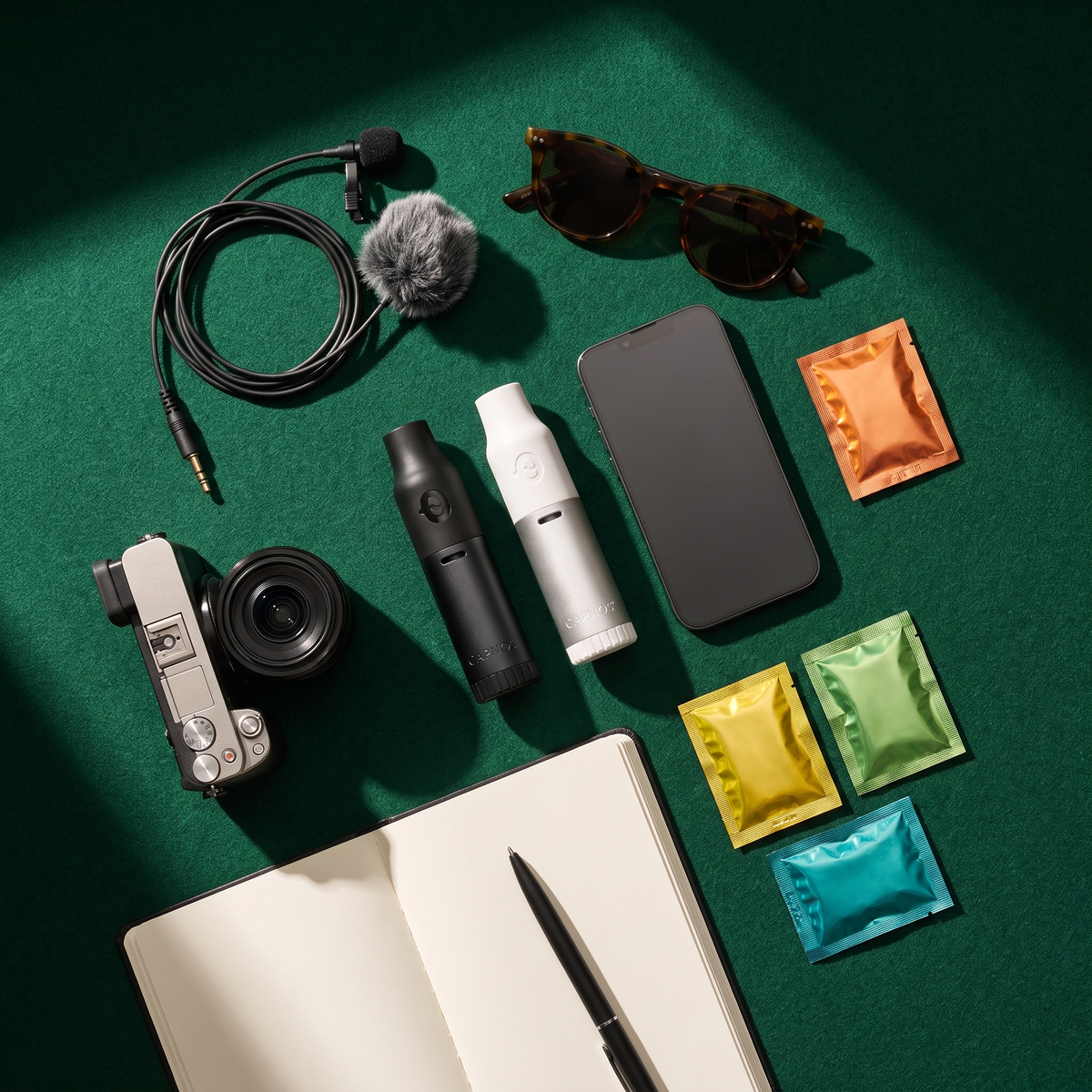 A creator kit laid out on green felt: a CAPNOS Legura and BRE-Z, camera, microphone, phone and flavor packs.